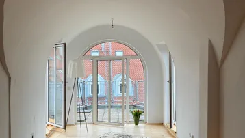 Helles Wohnzimmer mit gewölbter Decke, Holzboden und Zugang zu einem französischen Balkon.
