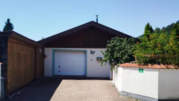Vorderansicht eines Einfamilienhauses mit integrierter Garage, gepflasterter Einfahrt und Satteldach.