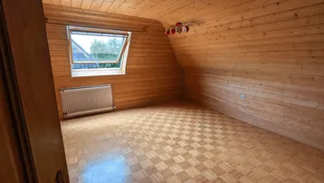 Gemütliches Zimmer im Dachgeschoss mit Holzverkleidung, Parkettboden und Dachfenster.