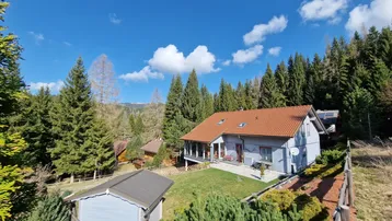 Charmantes Haus in den Bergen mit rotem Ziegeldach und umgebendem Wald unter blauem Himmel.