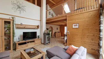 Geräumiges Wohnzimmer mit hohen Decken, Holzbalken und einem gemütlichen Kaminofen, offen zur Galerie.