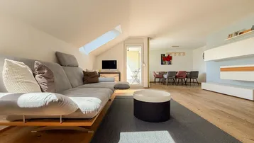 Helles und geräumiges Wohn-Esszimmer mit Dachschrägen, Holzboden und Zugang zum Balkon.