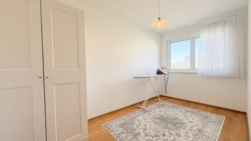 Helles Zimmer mit Holzboden, weißem Kleiderschrank und Fenster mit Bergblick.