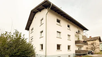 Weißes Mehrfamilienhaus mit mehreren Etagen und Balkonen unter bewölktem Himmel.