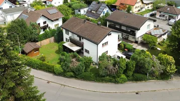 Luftaufnahme eines Einfamilienhauses mit Garten und umliegender Wohnbebauung in grüner Umgebung.
