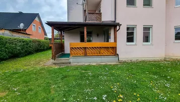 Überdachte Terrasse mit Holzzaun und Zugang zum Gartenbereich des Gebäudes.