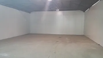 Geräumiger, leerer Lagerraum mit Betonboden und hoher Decke, beleuchtet von einer einzelnen Deckenlampe.