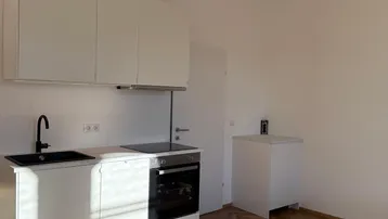 Moderne Einbauküche mit weißen Schränken, schwarzer Spüle und Induktionskochfeld, auf hellem Parkettboden.