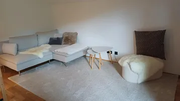 Helles Wohnzimmer mit einem bequemen Ecksofa, weichem Teppich und minimalistischen Beistelltischen.