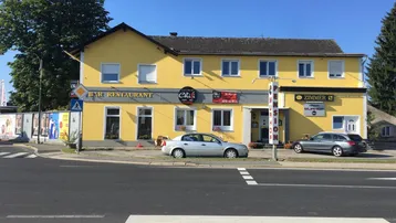 Gelbes Gebäude an einer Straßenecke mit Bar, Restaurant und Pension, umgeben von parkenden Autos.