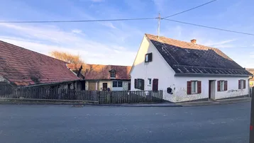 Altes Wohnhaus mit Satteldach und angrenzenden Nebengebäuden an einer ländlichen Straße.
