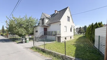 Weißes Einfamilienhaus mit Satteldach, kleinem Balkon und Vorgarten an einem sonnigen Tag.