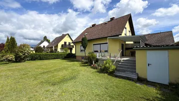 Gelbes Einfamilienhaus mit großem Garten und Terrasse unter blauem Himmel.