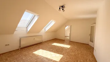 Helles Zimmer im Dachgeschoss mit Parkettboden und schrägen Wänden, ideal als Wohn- oder Schlafbereich.