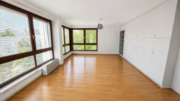 Helles Zimmer mit Holzboden, großen Fenstern und integrierten weißen Einbauschränken.