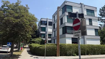 Mehrstöckiges Wohngebäude mit moderner Architektur, umgeben von Bäumen und Hecken.