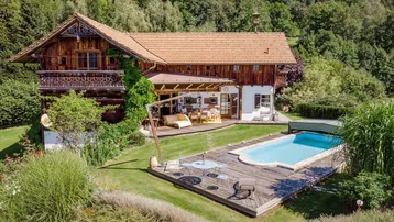Großzügiges Anwesen mit traditionellem Holzhaus, Pool, Sonnenterrasse und üppigem Garten in grüner Umgebung.