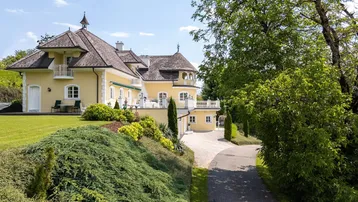 Elegante Villa mit gelber Fassade, weitläufiger Auffahrt und gepflegtem Gartenbereich.