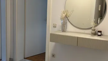 Heller Eingangsbereich mit Fliesenboden, einem runden Spiegel und einer schwebenden Konsole.