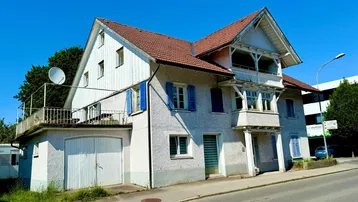 Historisches Wohnhaus mit blauen Fensterläden, Garage und Balkon unter strahlend blauem Himmel.
