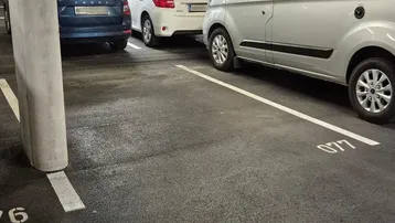 Tiefgarage mit mehreren geparkten Fahrzeugen, Betonstützen und Deckenbeleuchtung.