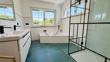 Modernes Badezimmer mit Doppelwaschbecken, Badewanne und einer geräumigen begehbaren Dusche, hell durch große Fenster.