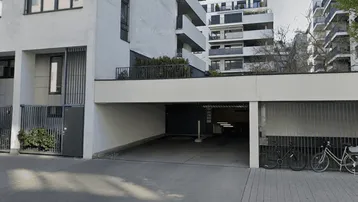 Eingangsbereich einer modernen Wohnanlage mit Zufahrt zur Tiefgarage und Balkonen in den oberen Etagen.