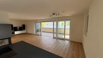 Heller Wohnbereich mit Holzboden und breiter Schiebetür zum Balkon, ideal für Entspannung.