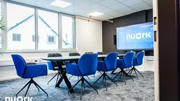 Heller Konferenzraum mit großen Fenstern, langem Tisch und blauen Stühlen, ideal für Besprechungen.