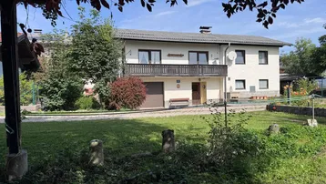 Zweistöckiges Wohnhaus mit Balkon und integrierter Garage, umgeben von einem grünen Gartenbereich.