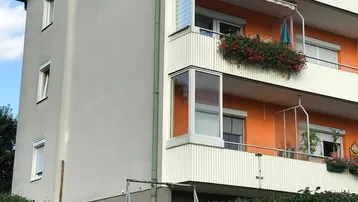 Mehrstöckiges Gebäude mit Balkonen, Blumenkästen und orangefarbenen Akzenten an der Fassade.