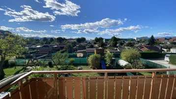 Balkon mit weitem Blick über Gärten, Wohngebiet und die umliegende Berglandschaft unter blauem Himmel.
