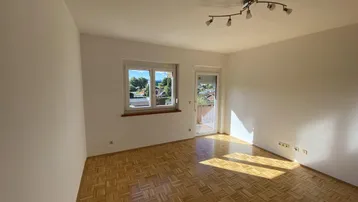 Helles Zimmer mit Parkettboden und Zugang zu einem Balkon, durchflutet von natürlichem Sonnenlicht.