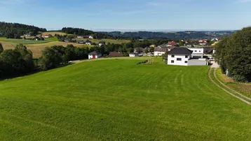 Weitläufige Landschaftsaufnahme mit grünen Feldern, vereinzelten Häusern und einem Dorf in der Ferne.