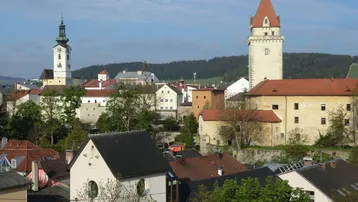 Panoramablick über eine historische Stadt mit Kirchturm und Burgturm unter blauem Himmel.