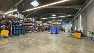 Geräumige Lagerhalle mit hohen Decken, Betonboden, Regalsystemen und natürlichem Lichteinfall durch Oberlichter.