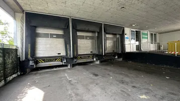Laderampenbereich mit drei Rolltoren und einer Zufahrtsrampe für Lieferfahrzeuge unter einer Betonüberdachung.
