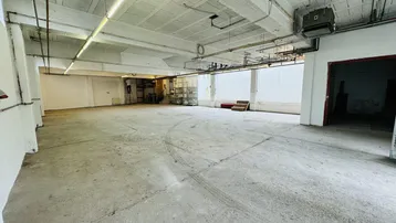 Großer, leerer Lagerraum mit Betonboden, hohen Decken und sichtbaren Installationen, bereit zur Nutzung.
