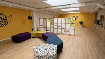 Geräumiger Loungebereich mit farbenfrohen Sitzgelegenheiten, Holzfußboden und Oberlichtern für natürliches Licht.