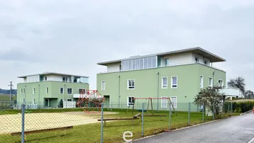 Zwei moderne Mehrfamilienhäuser mit Spielplatz in einer ländlichen Umgebung.