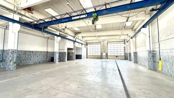 Geräumige Lagerhalle mit Betonboden, Oberlichtern und einem blauen Kran, bereit für industrielle Nutzung.