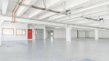 Großer, leerer Lagerraum mit hohen Decken, Betonboden und sichtbaren Installationen an der Decke.