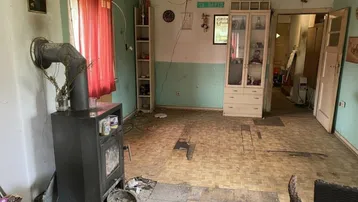 Wohnzimmer mit Holzofen, abgenutzten Wänden und einfacher Einrichtung, bereit für Renovierung.