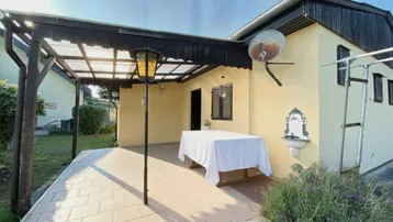 Überdachte Terrasse mit Fliesenboden und einem Tisch, ideal für Mahlzeiten im Freien.