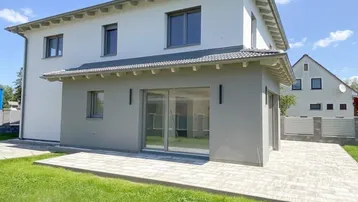 Modernes Einfamilienhaus mit heller Fassade, grauen Akzenten und großer Glasfront zum Garten.