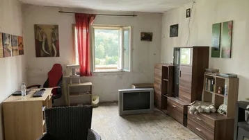 Abgenutztes Wohnzimmer mit alten Möbeln, einem Schreibtisch und Blick ins Grüne.