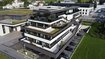 Moderne Bürogebäude-Architektur mit gestuften Etagen, Gründächern und großen Glasfassaden in einer ländlichen Umgebung.
