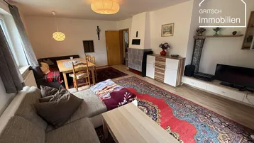 Gemütliches Wohnzimmer mit Sofa, Couchtisch und einem traditionellen Kachelofen, dekoriert mit Teppichen.