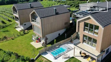 Luftaufnahme von modernen Häusern mit Pool, umgeben von Weinbergen und grüner Landschaft.