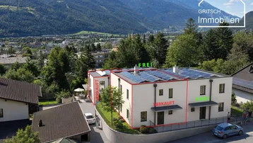 Luftaufnahme von modernen Gebäuden mit Solaranlagen und Bergblick in einer Wohngegend.